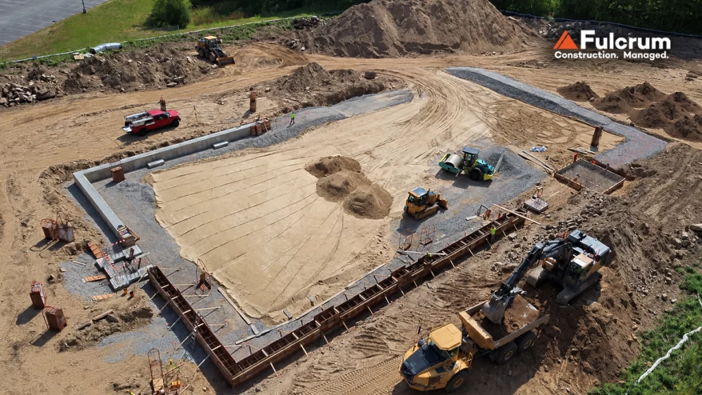 Aerial drone view of sitework and foundation construction at EPSI's new 27,000-square-foot manufacturing facility in Derry, NH, showing concrete foundation walls, excavation, and construction equipment.